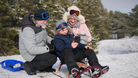 Family Vacation Cute Male Child with Elderly Woman and Man Have Fun Sledding in Snowy Meadow and