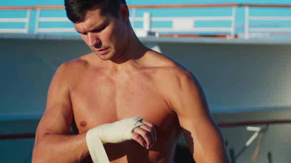 Athletic Handsome Man with Naked Torso Puts on Hands Wraps for Boxing Workout Outdoor