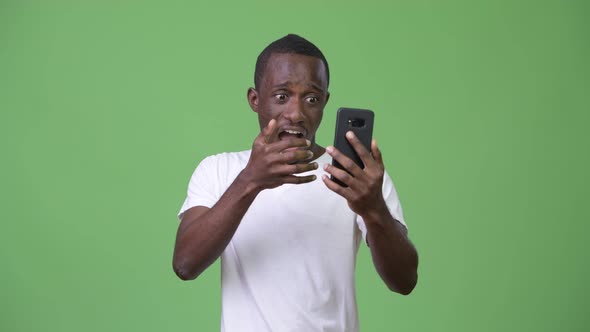 Young African Man Looking Shocked While Using Phone alt
