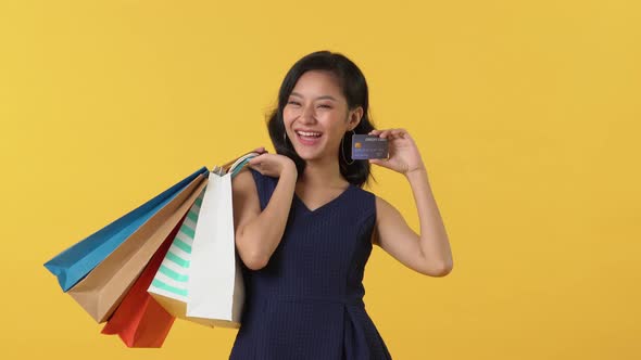 Happy young Asian woman showing credit card while holding colorful shopping bags