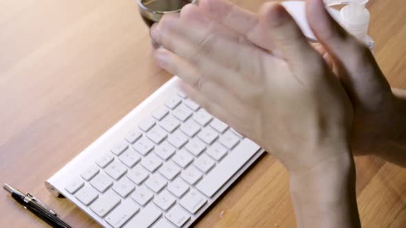 Person cleaning her hands with sanitizer at work above a laptop computer at a small office during th alt