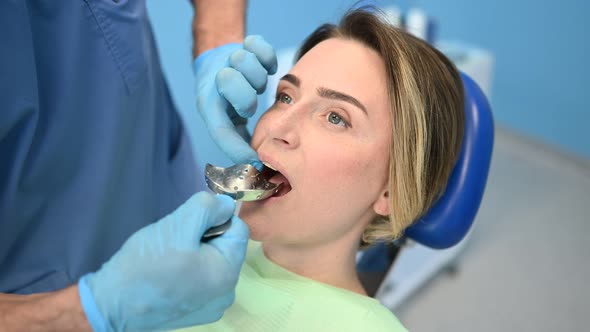 Dentist examining a patient's teeth using dental equipment impression spoon in dentistry office. 