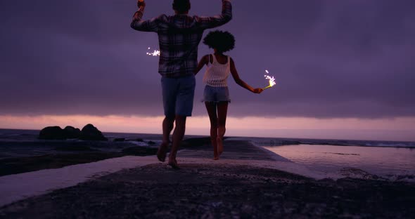 Couple running with sparklers on concrete pier at beach 