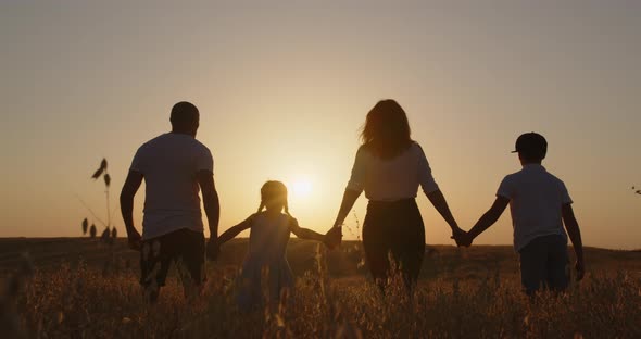Happy Family With Children Having Fun Jumping In The Field At Sunset