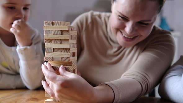 Happy mom playing with children in game. parent helps to build tower of blocks. alt