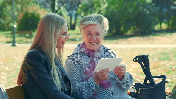 Middle Close Up of Old Woman Reading a Letter to Pretty Young Woman in Park alt