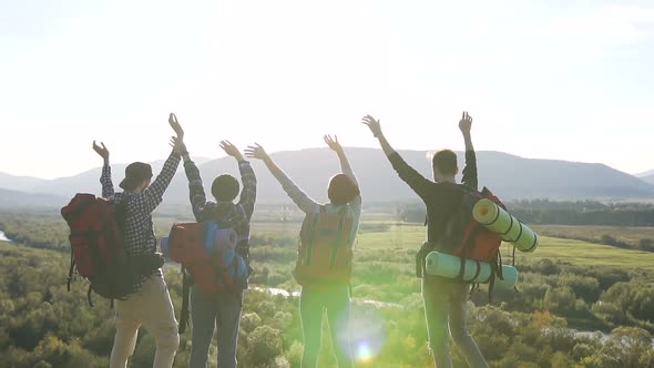 Two Couples of Young Travelers Waving at the Top of a Mountain alt