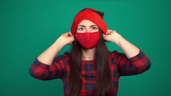 Woman Wearing Red Medical Face Mask Putting on Santa Hat.