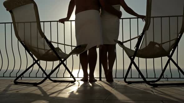 Couple in Love Stands Hugging on the Terrace and Admires the Sunset Over the Sea alt