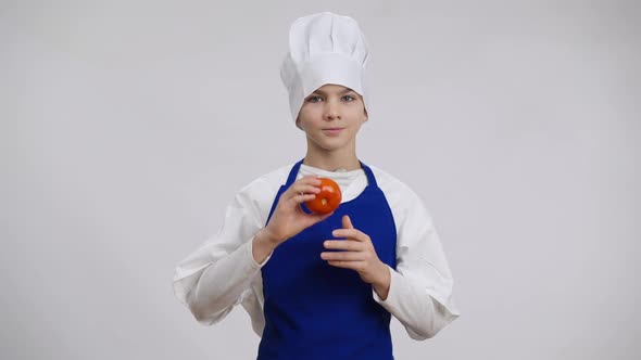 Positive Handsome Caucasian Boy in Chef Uniform Posing Closing Eye with Tomato alt