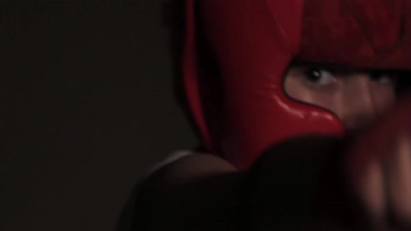 Young guy boxer in a red protective helmet posing at the camera close-up in bandages