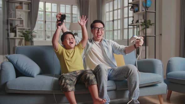 Asian Man And Son Win Playing Video Game, Hands Up While Winning Video Game alt