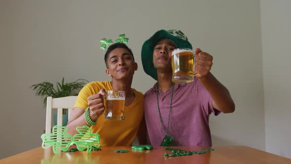 Mixed race gay male couple making st patrick's day video call raising glasses wearing costumes alt