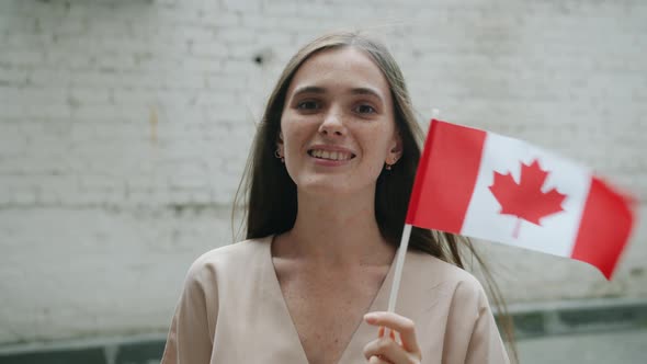 Slow Motion Portrait of Cute Young Female Student Holding Canadian Flag Outdoors on Brick Wall alt