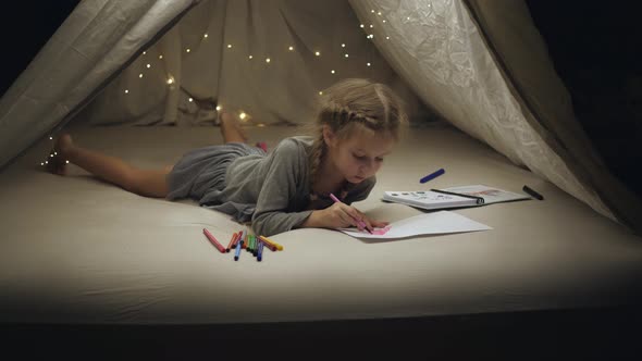 A Little Girl in a Makeshift Hut Draws on a White Piece of Paper