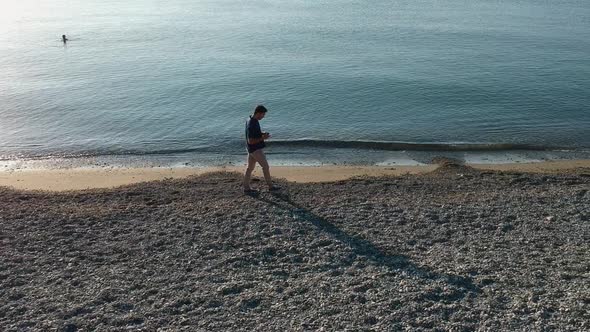 Aerial Shot of Man Walking By the Sea and Texting