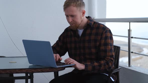 caucasian man working on laptop while sitting on balcony