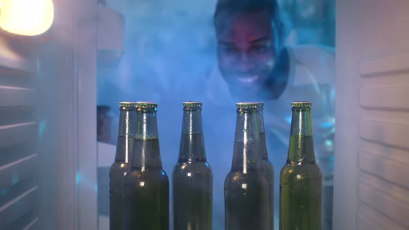 African Guy Taking Bottle of Beer From Refrigerator alt