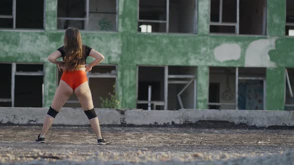 Girl Dances Twerk on the Roof of an Abandoned Building. Girl in Red Shorts and Tights in a Cell