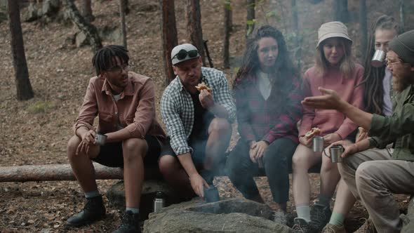 Portrait of Cheerful Youth Eating Around Fire in Forest Chatting Laughing with Dog Running Around alt