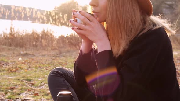 Slow Motion Caucasian Blonde Woman with Beige Hat in Black Sweater Drinks Hot Tea From Thermos in alt