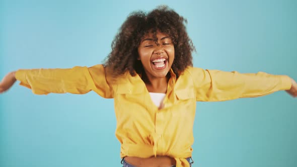 Young Afro American Woman Laughing Jumping Up Spreading and Raising Her Hands While Posing on Blue alt