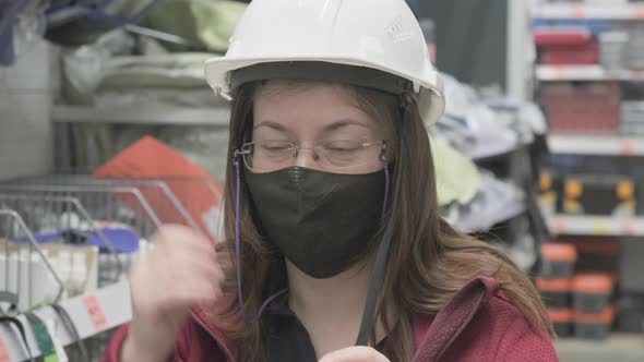 Woman in a Building Materials Store Measures on a White Safety Helmet