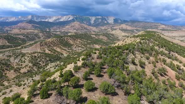 Aerial Over Top of Sandy Desert Mountains with Mountain Range and Storm in Distance alt