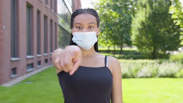 A Young Black Woman in a Face Mask Points at the Camera and Nods - an Office Building alt