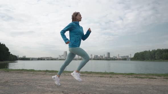 Slow Motion Young Sportswoman in Sportswear Trains in a Park Near the River