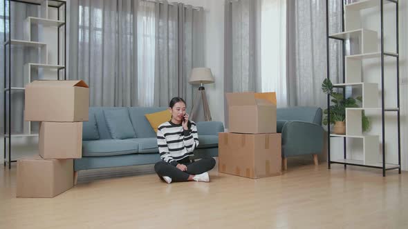 Young Asian Woman With Cardboard Boxes Talking On Smartphone After Moving Into A New House  alt