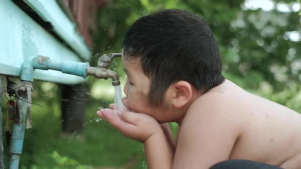 Slow motion of Asian boy drinking outdoors fresh water from tap, Saving water concept. alt