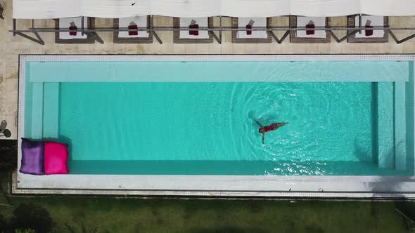 Female swimming face up at Shore Amora Canggu Hotel pool in Bali, Indonesia, Aerial top view shot alt