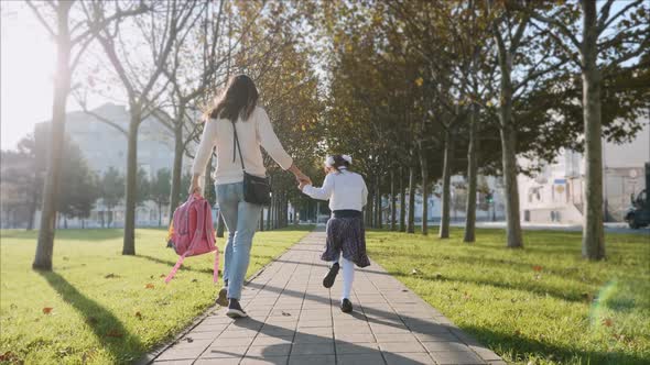 A Woman and Little Girl in School Uniform Running in Park, Steadicam, Back View