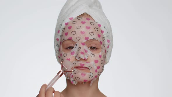 Lovely Young Smiling Child Girl Applying Cosmetic Moisturizing Face Mask Use Massage Roller alt