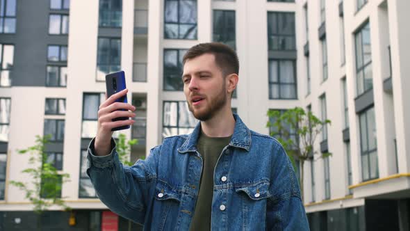Angry Caucasian Man Talking During Video Chat on Smartphone Outside Office alt