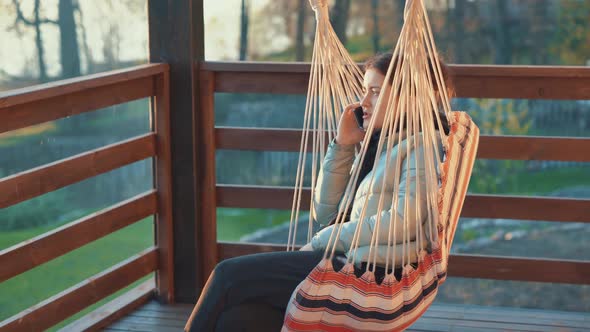 A Young Woman Talking on the Phone with Friends Sitting on the Veranda Admiring the Sunset