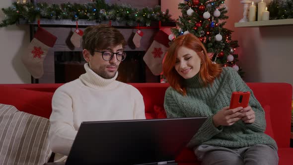 Man and woman. having fun using technology at home. Girl and guy talking, laughing, looking at lapto alt