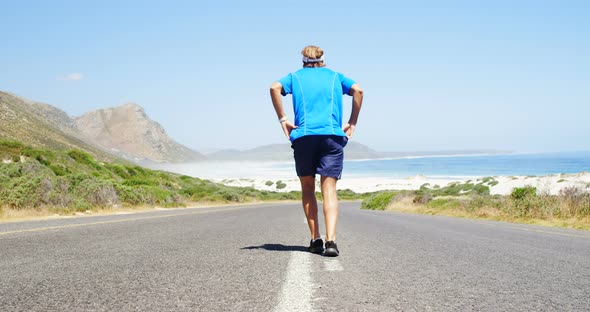 Rear view of triathlete man jogging in the countryside road alt