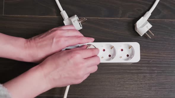 Close-up of a female hands turns off the plug out of socket. The power strip is on the floor.