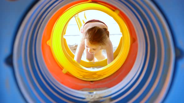 3 year old girl plays in a colorful tube on the beach.