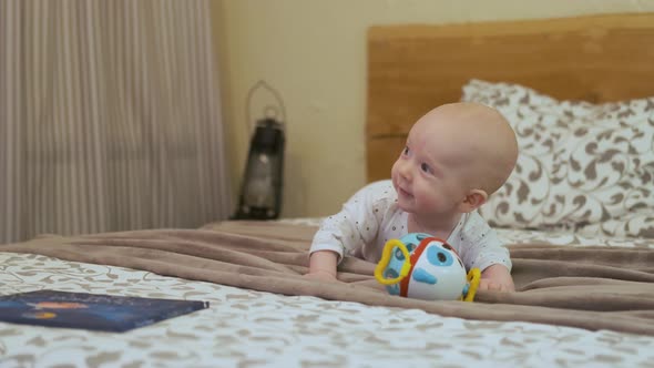 joyful baby lies on the bed next to the toy