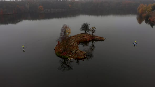 Drone Shot of Man and Woman on Sup Paddle Boards at Wide River on Golden Autumn Forest Background alt