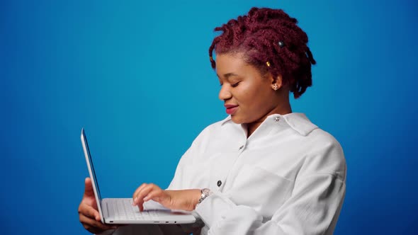 Young Afro Woman Holding Laptop and Typing Against Blue Background