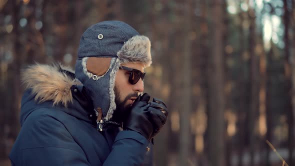 Man Warms Hands Blows Steam From Mouth In Frost Winter Forest Cold Breath. alt