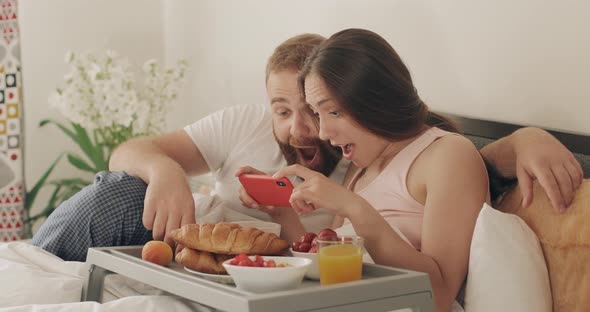 Man and Woman Making Big Eyes While Looking Shocked About Unbelievable News on Smartphone alt
