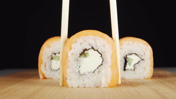 Human Hand Takes a Sushi by Chopsticks from A Wooden Plate