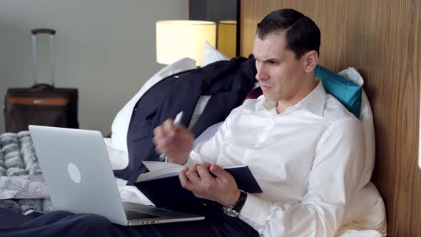 Businessman in a Hotel Room Taking Notes in the Diary