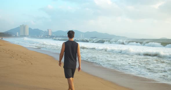 Man Walking Along the Sand Along the Coast in the Open Air Against the Backdrop of the Beautiful Sea alt