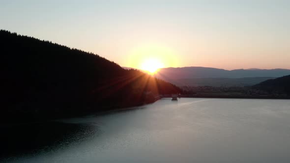 Aerial crane shot of sun setting behind ridge over picturesque mountain lake alt